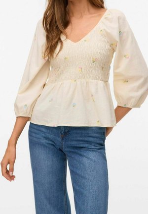 Witte blouse met bloemenborduursel, V-hals, gerimpeld lijfje en pofmouwen. Gecombineerd met blauwe rechte jeans.