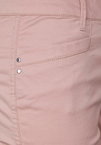 Ljusrosa denim med en slät textur och synliga stygn. Har en ficka med silverfärgade metalldetaljer.