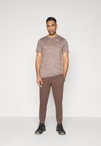 Camiseta deportiva marrón con una textura sutil y un logo blanco de Nike, combinada con joggers marrones y zapatillas deportivas negras.