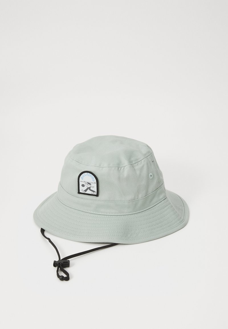 Hellegrüner Bucket Hat aus Stoff, mit einem runden Aufnäher an der Vorderseite und einem verstellbaren schwarzen Kinnriemen. Texturierte Oberfläche und breiter Rand.