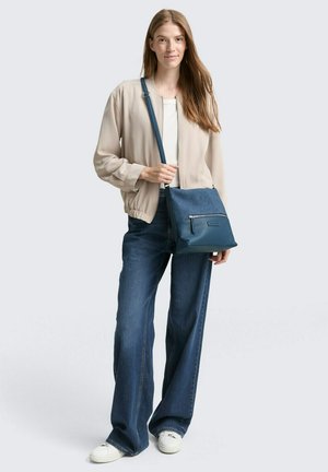 Sac en coton avec une texture en denim et des accents en cuir teal. Dispose d'une poche zippée à l'avant et d'une bandoulière ajustable.