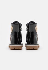 Botines de charol negro con detalles en forma de corazón dorado texturizado, una suela de goma marrón y una cremallera lateral para facilitar su uso.