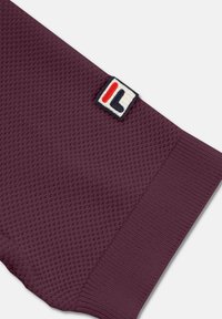 Tessuto borgogna con texture e polsino a costine, caratterizzato da un logo ricamato rettangolare in rosso, bianco e blu sul lato.