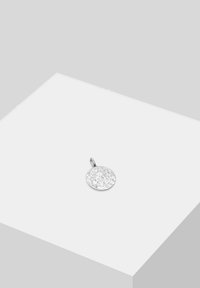 Pendentif rond en argent avec une surface texturée, présentant une petite boucle pour attache. Exposé sur un piédestal blanc sur fond gris.