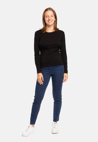 Top fitted a maniche lunghe nero, jeans skinny blu scuro e sneakers bianche. L'outfit presenta un design semplice e texture morbide.