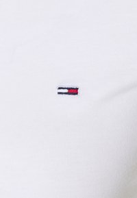 Litet rektangulärt rött, vitt och blått broderat märke på en enkel vit ribbad tyg, troligtvis en del av ett plagg.