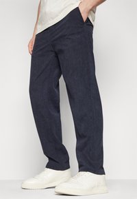 Marineblaue Cordhosen mit lockerer Passform, ausgestattet mit Seitentaschen und einer strukturierten Oberfläche. Kombiniert mit weißen Turnschuhen.