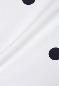 Tela blanca con grandes lunares azul marino, textura suave y un ligero brillo, mostrando una esquina doblada para detalle.