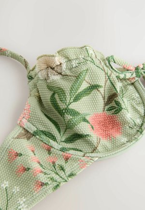 Žalias veido kaukės su gėlių raštu, pagamintas iš tekstūruotos medžiagos, kuriame pavaizduoti rožiniai ir balti gėlės motyvai, su reguliuojamomis ausų kilputėmis ir kontūruota forma.