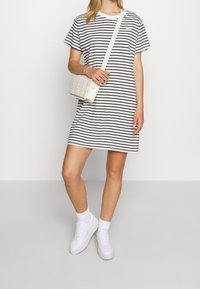 Raidallinen t-paitamekko valkoisena ja mustana, jossa lyhyet hihat ja rento istuvuus. Yhdistetty tekstuuroituun valkoiseen olkalaukkuun ja valkoisiin tennareihin.