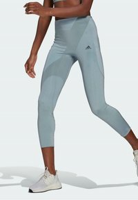 Wysokiej talii, jasnoniebieskie legginsy o gładkiej teksturze. Posiadają tonalne wzory oraz logo Adidas na lewym udzie.