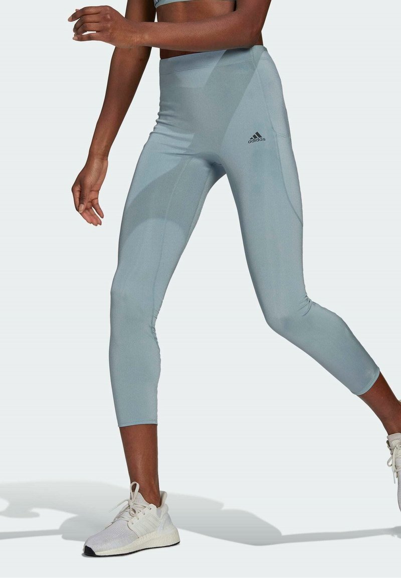 Wysokiej talii, jasnoniebieskie legginsy o gładkiej teksturze. Posiadają tonalne wzory oraz logo Adidas na lewym udzie.