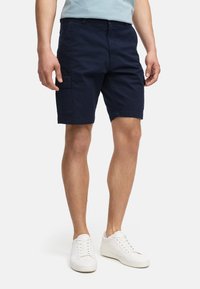 Tengeri cargo short, pamutból készült, oldalzsebekkel, egyenes szabású, felhajtott szegéllyel, fehér tornacipővel viselve. Sima textúra.