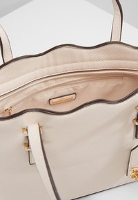 Beige handbag with a textured surface, scalloped top edge, gold-tone hardware, and an interior zip pocket. Smooth inner lining.