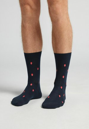 Calcetines navy con una textura suave, decorados con patrones dispersos de cabezas de alienígenas rojas. Puños acanalados para un ajuste seguro sobre el tobillo.