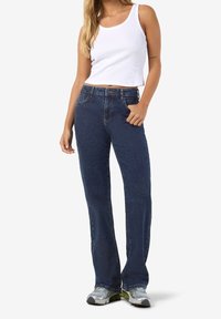 Modré džíny z denimu s rozšířenými nohavicemi, středním pasem a pěti kapsami. Kombinovány s bílým žebrovaným tílkem a šedými teniskami.