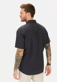 Zwarte korte mouw shirt gemaakt van een gestructureerde stof, met een button-down kraag en een klein accentdetail op de achterkant.