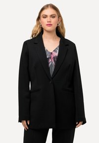 Blazer negro con un corte estructurado, cierre de un botón y dos bolsillos frontales. La tela parece suave con un acabado mate.