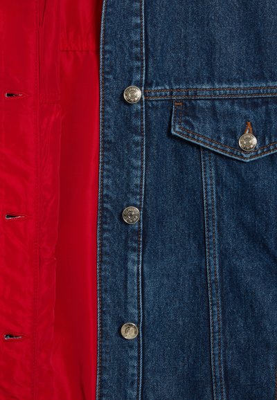 Teksajakett ereda punase siseküljega, millel on hõbedased nupud, terav rinnatasku ja kontrastsed tekstuurid välisteks denim ja sisepinna vahel.