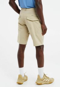 Lichtbeige shorts met een relaxte pasvorm, elastische tailleband en meerdere zakken, gecombineerd met lichtgekleurde sportschoenen en sokken.
