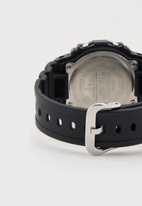 Must kummist rihmaga käekell, millel on hõbedane pandlaga, ümmargune metallkorpus ning graveeritud roostevabast terasest tagakülg, millel on "Stranger Things" logo.