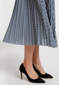 Décolleté neri in suede con punta affusolata, abbinati a una gonna plissettata con strisce diagonali blu e bianche.