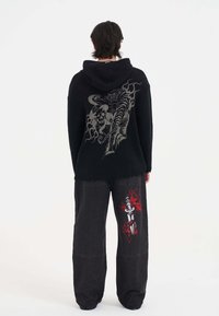 Felpa nera a coste con una grande grafica argento sul retro, abbinata a pantaloni larghi neri con grafiche di spade rosse e bianche.