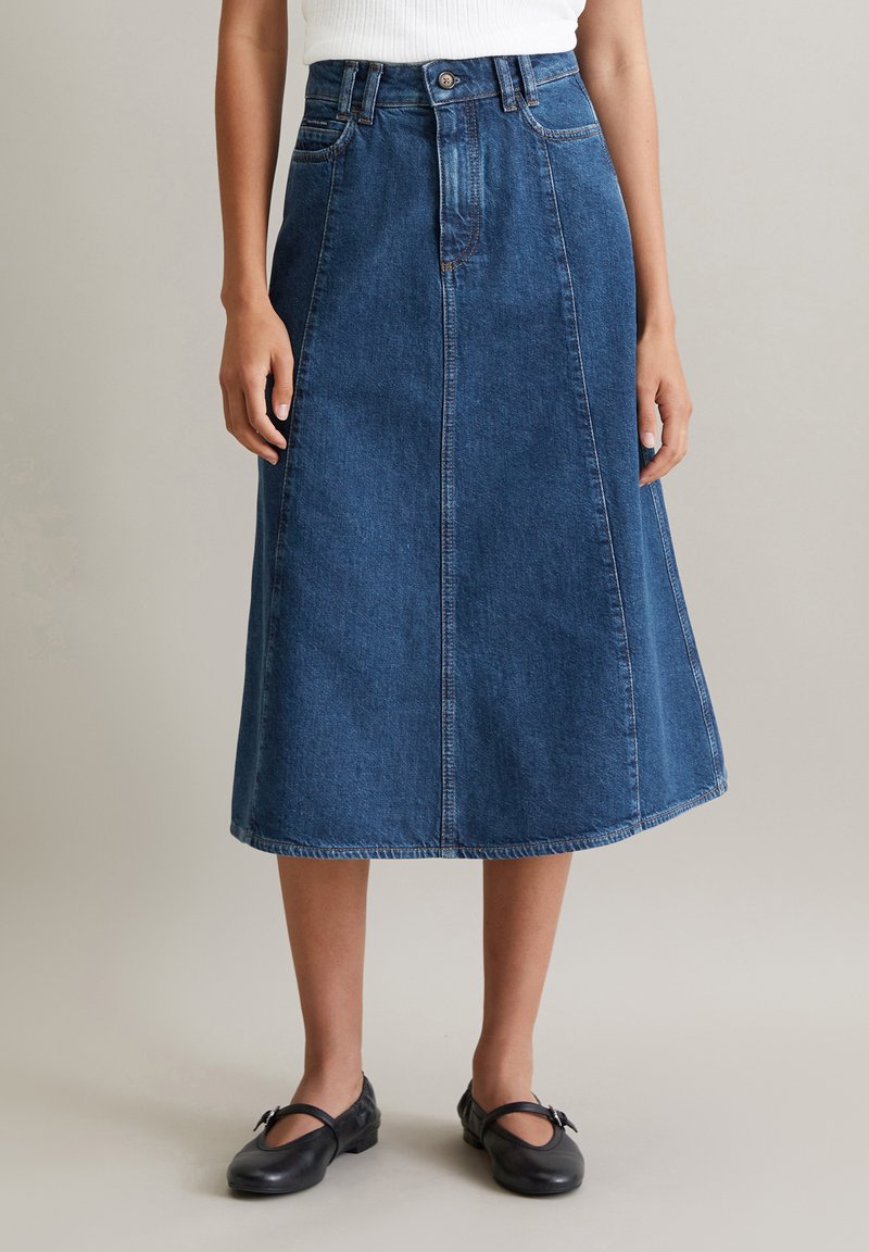 Jupe midi en denim bleu foncé, avec une taille haute, un détail de couture à l'avant et une silhouette en A. Complétée par des coutures discrètes et une fermeture à bouton.
