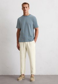 T-shirt à manches courtes rayé bleu, pantalon en lin léger et ample, et chaussures à lacets couleur beige. Design simple avec les ourlets des pantalons retroussés.
