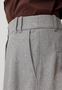 Szare wełniane spodnie o teksturowanym wykończeniu, z wysokim stanem, fałdami z przodu oraz detalem kieszeni po boku.