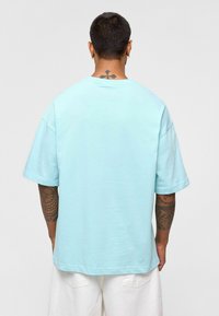 T-shirt en coton bleu clair avec une coupe décontractée, des manches courtes et un col rond côtelé, présentant une couture au dos et des coutures visibles.