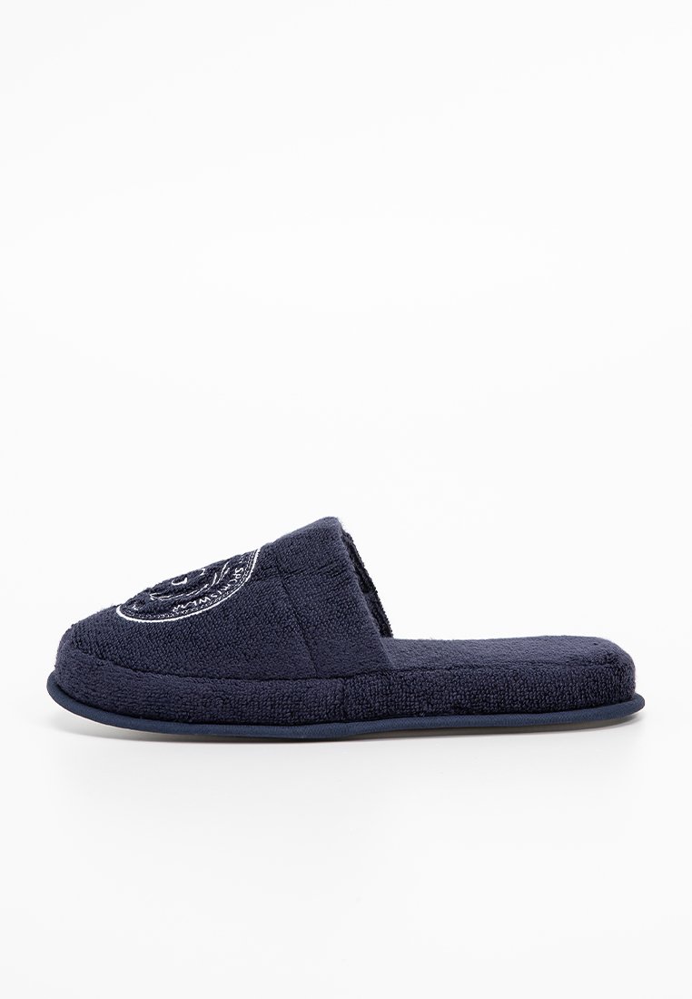 Marineblaue Hausschuhe aus weichem Frottee-Material, mit einem offenen Zehendesign und einem gestickten Logo auf der Vorderseite. Rutschfeste Sohle.