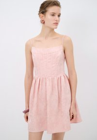 Vestido rosa claro con cuerpo ajustado, tirantes finos y falda recogida. Presenta una textura floral y un brillante sutil en toda la tela.