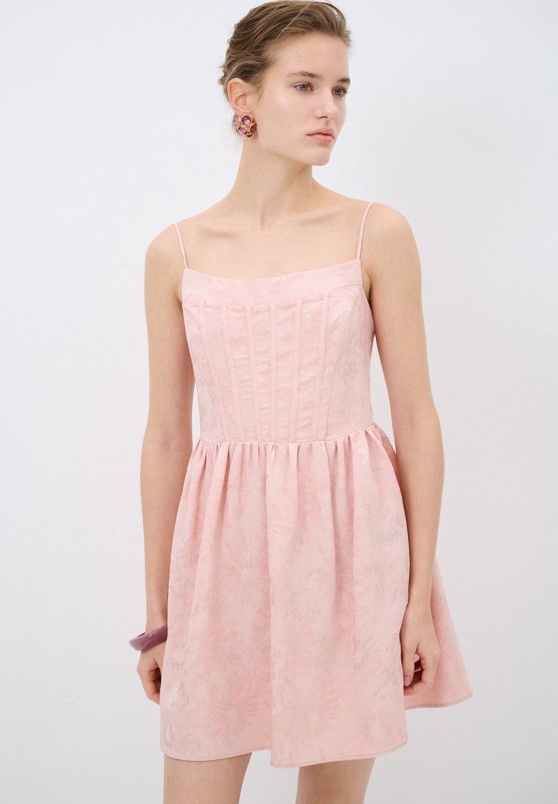 Vestido rosa claro con cuerpo ajustado, tirantes finos y falda recogida. Presenta una textura floral y un brillante sutil en toda la tela.
