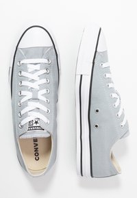 Baskets en toile grises avec lacets blancs, embout en caoutchouc, bande noire le long de la semelle et œillets pour la ventilation. Design basse classique.