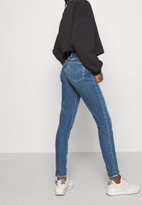 Vaqueros de denim azul con ajuste slim, que presentan una cintura alta, costuras contrastadas y un logo clásico de la marca en los bolsillos traseros.