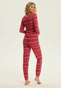 Czerwony zestaw piżam z wzorem płatków śniegu, wykonany z miękkiego materiału, z długimi rękawami i dopasowanymi mankietami przy kostkach. W stylu retro.