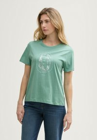 T-shirt vert à manches courtes en coton doux, avec un design graphique blanc au centre. Coupe décontractée avec un col rond.
