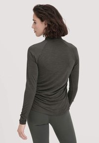 Dunkelgraues Langarmoberteil mit hohem Kragen, ausgestattet mit Raglanärmeln und einem gerafften Rückendetail. Weicher Stoff und figurbetonendes Design.