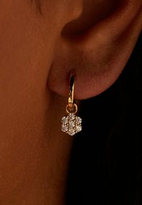 Gouden oorring in de vorm van een hoepel met een bloemmotief en kleine heldere kristallen in een cluster. Close-up weergave die textuur en glans benadrukt.