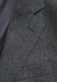 Blazer grigio in lana con superficie testurizzata, rever a scollatura e tasca singola sul davanti. Foderato con un materiale scuro e liscio.