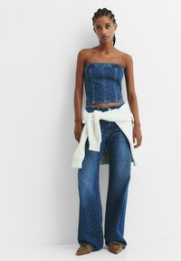 Top fără bretele din denim și blugi cu picioare largi, cu un model cu puncte, însoțite de un pulover ușor legat în talie. Pantofii maro completează look-ul.