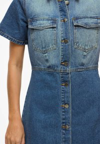 Denimkleit lühikeste varrukatega, kahe rinnahoidjaga ja esise nupu sulgemisega. Omab gradient sinist värvi, kontrastsete õmbluste ja metalldetailidega.
