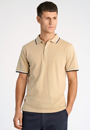 Polo beige en tissu texturé, doté d'une patte de boutonnage à trois boutons, de manches courtes et d'un col rayé noir et blanc.