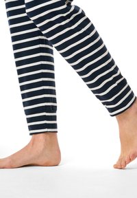 Mörkblå och vit randiga pyjamabyxor med mjuk textur, avsmalnande ben och ankellånga muddar. Barfota står på en vit yta.
