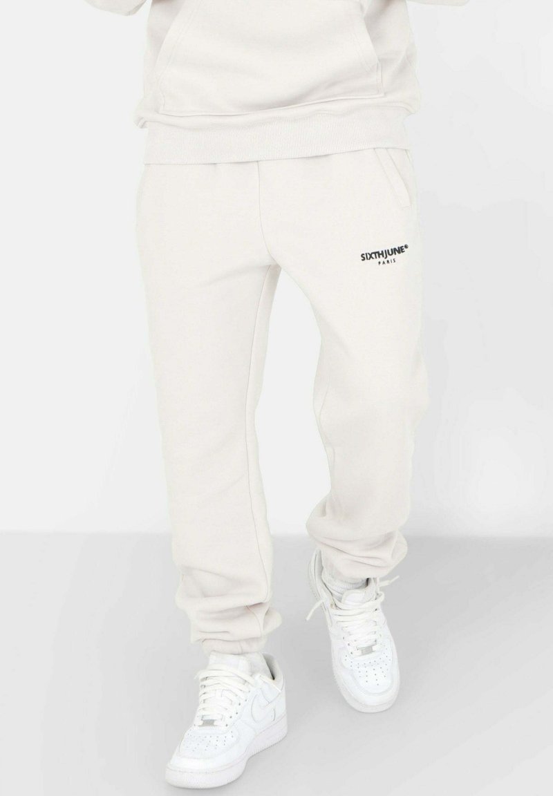 Lichtbeige sweatpants van zachte stof, voorzien van zijzakken en een klein zwart logo op het linkerbeen. Gecombineerd met witte sneakers.