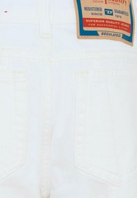 Witte spijkerbroek met een hoge taille, achterzakken en een bruine label met blauwe en rode tekst die merkdetails en wasinstructies aangeeft.