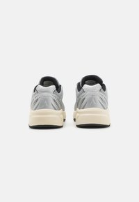 Sapatilhas atléticas cinzentas com um upper em malha, colarinho almofadado e sola em creme contrastante. Apresentam um design minimalista e uma brandagem subtil.