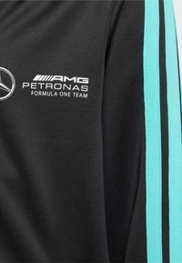 Top sportivo nero con strisce accento turchesi. Presenta loghi: AMG, PETRONAS e "Formula One Team" in bianco. Tessuto testurizzato.