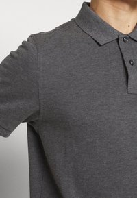 Polo gris en tissu texturé, col avec deux boutons et manches courtes, vue rapprochée de la moitié supérieure.